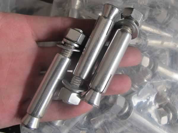 Three galvanized expansion anchors in a hand.